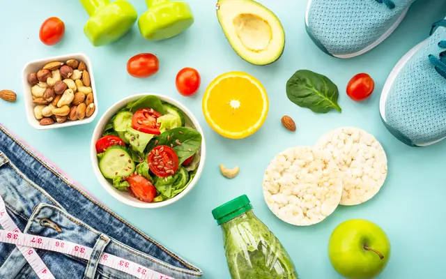 Fresh salad bowl with spinach, cucumber, tomatoes and flax seeds beside nuts and an orange